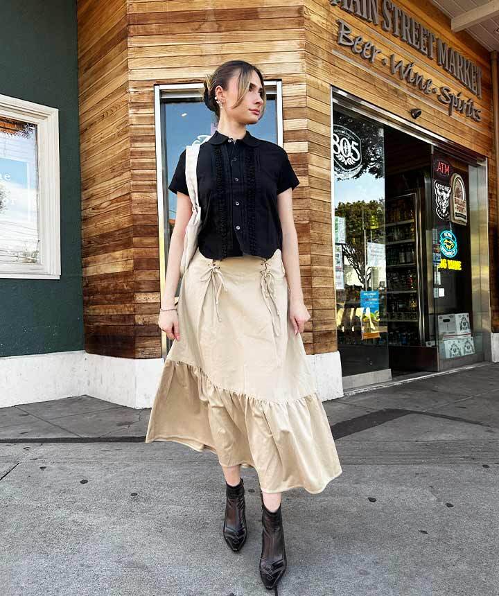 model posing behind a store, wearing black top and biege skirt